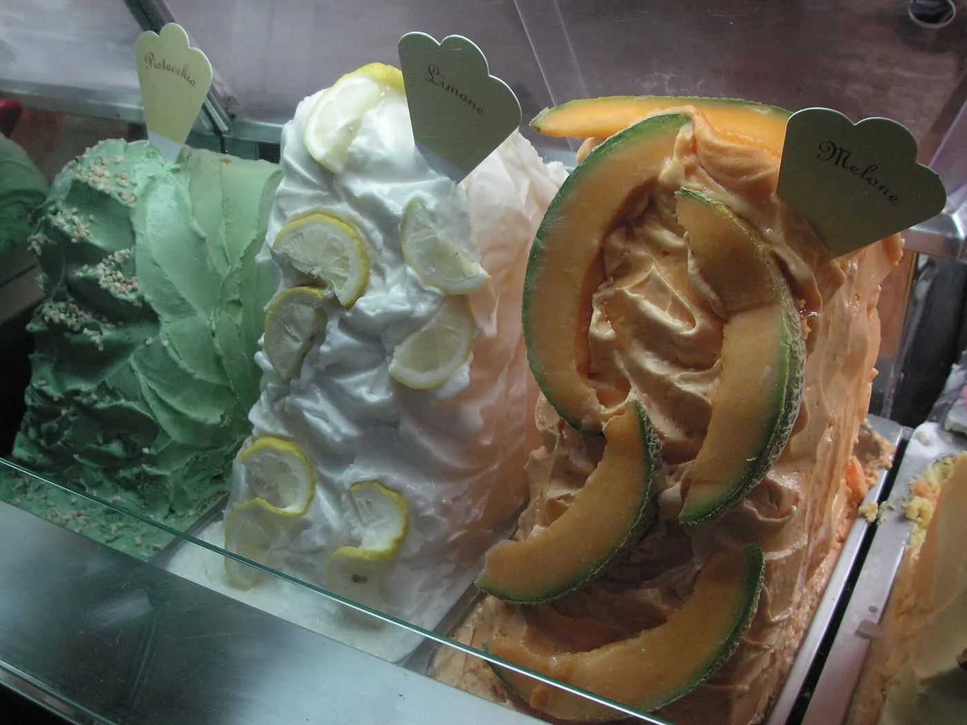 Green, lemon and melon gelato piled in a glass case, the lemon and melon decorated with slices of fruit