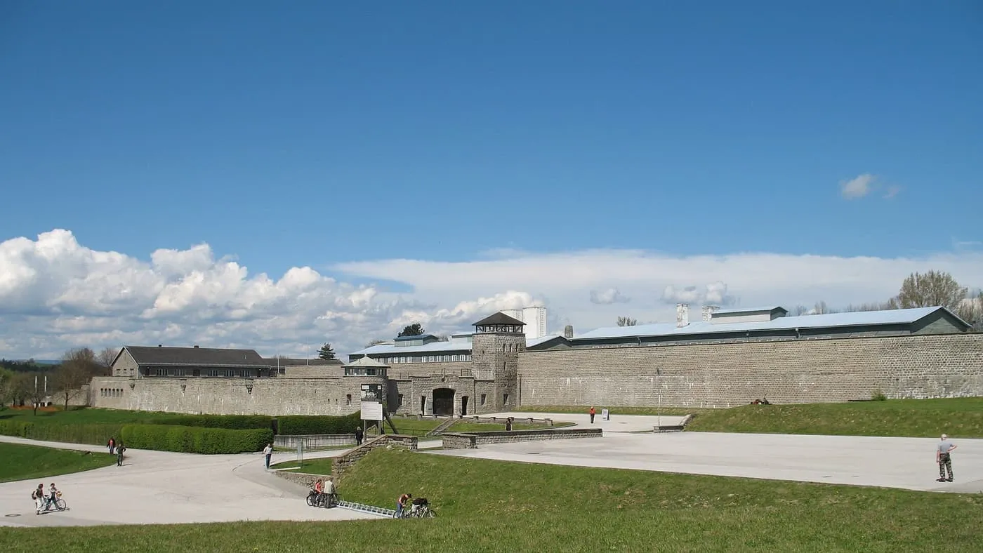 The long stone outer wall of the Mauthausen Memorial seen across a paved approach