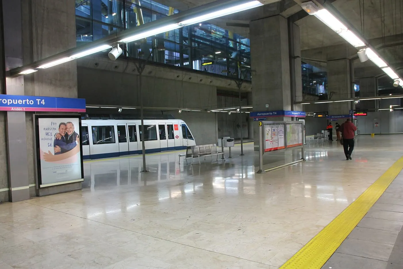 A white Metro train waiting at the platform of Aeropuerto T4 station, under a low concrete ceiling