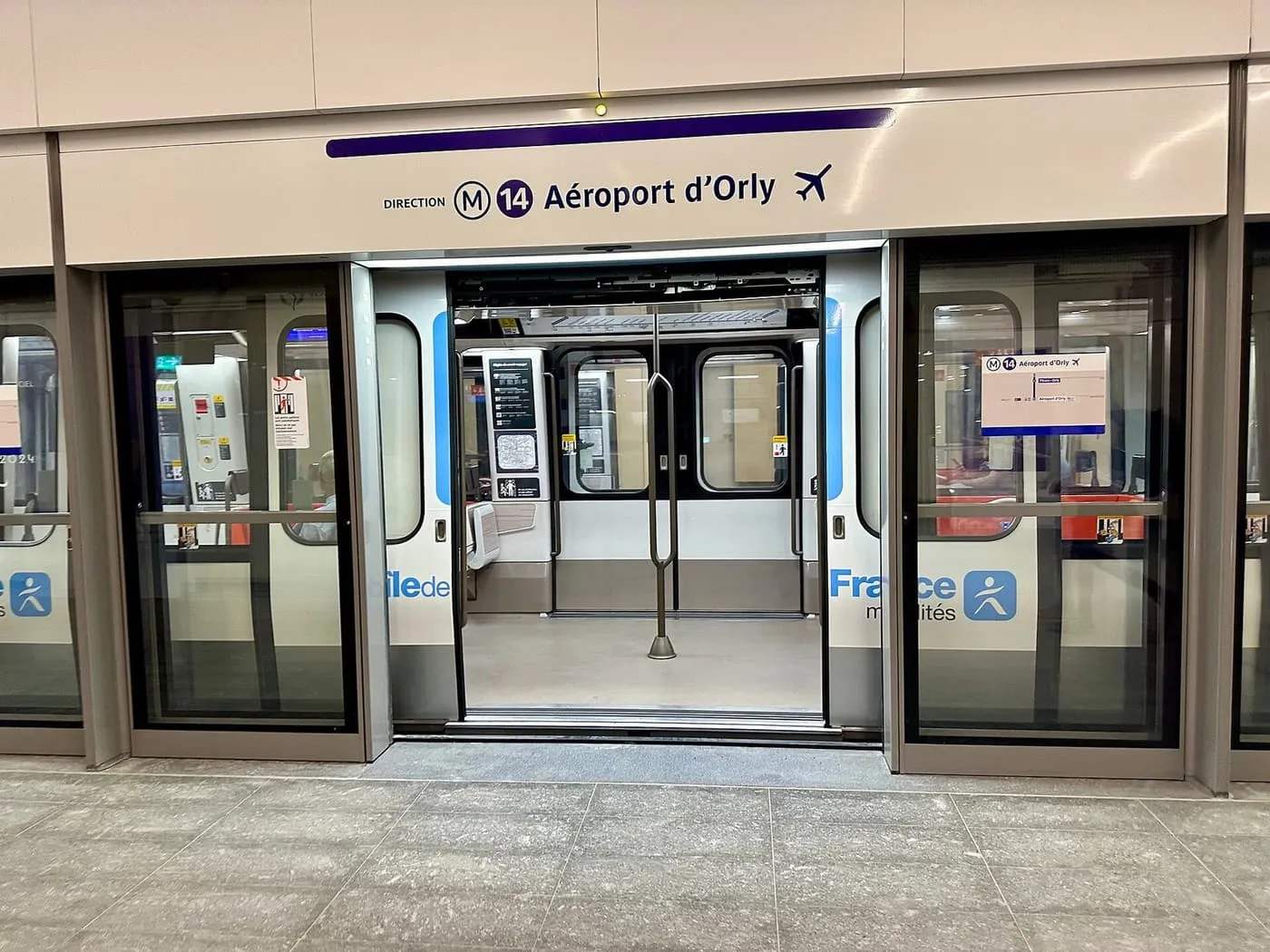 A line 14 metro train with its doors open behind platform screen doors, under a sign reading Direction Aéroport d'Orly