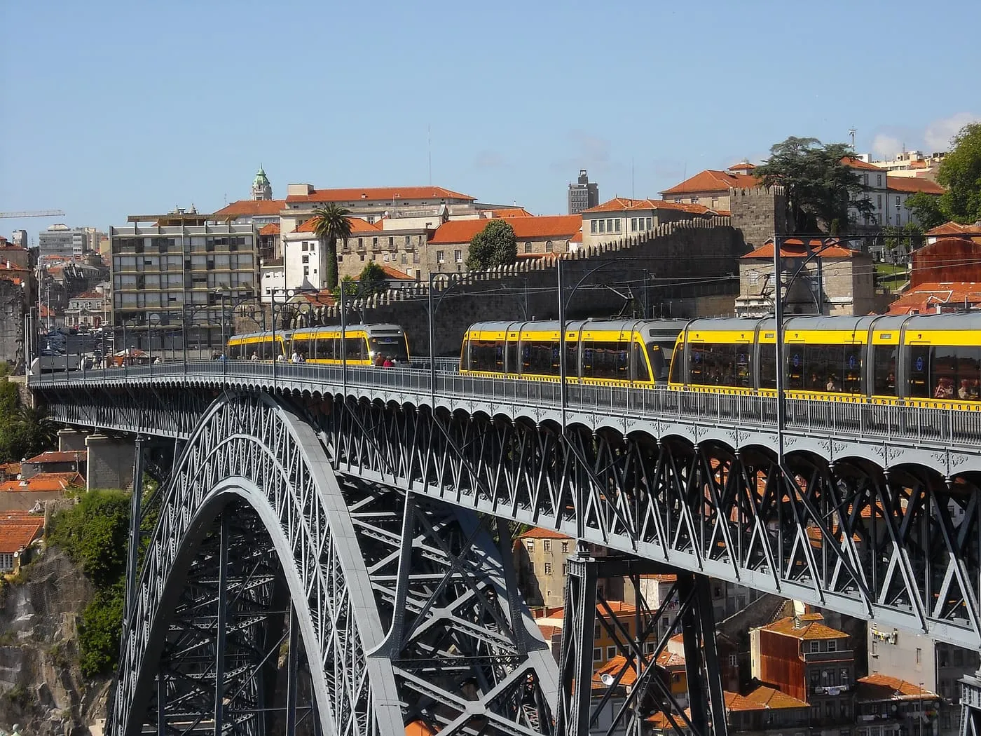 Two yellow Metro trains on the upper deck of the Dom Luís I bridge, with the old town rising behind