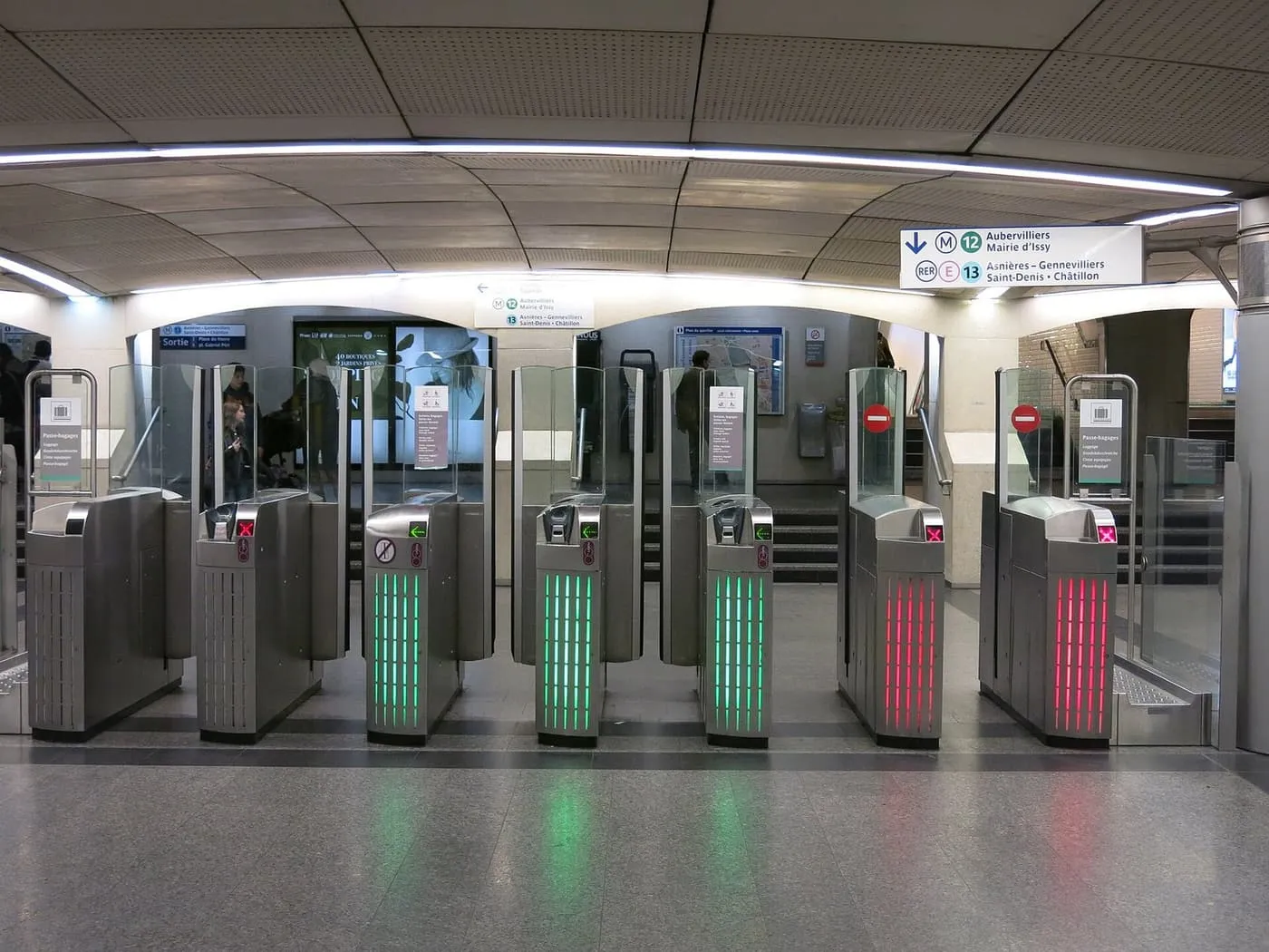 A row of metro ticket gates, some lit green for entry and others red, under signs for lines 12 and 13