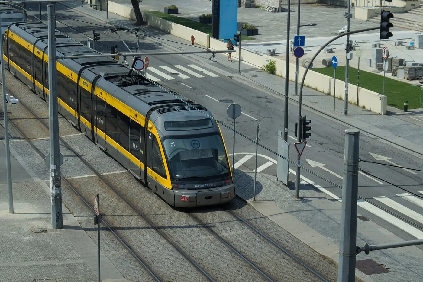 A yellow and grey Metro do Porto tram running along a cobbled street between overhead wires, seen from above