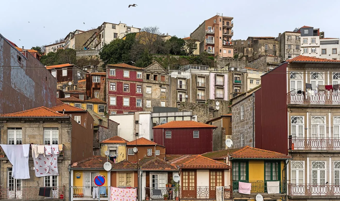 Red, yellow and white houses climbing a hillside above a street in Miragaia, with washing hung from the windows