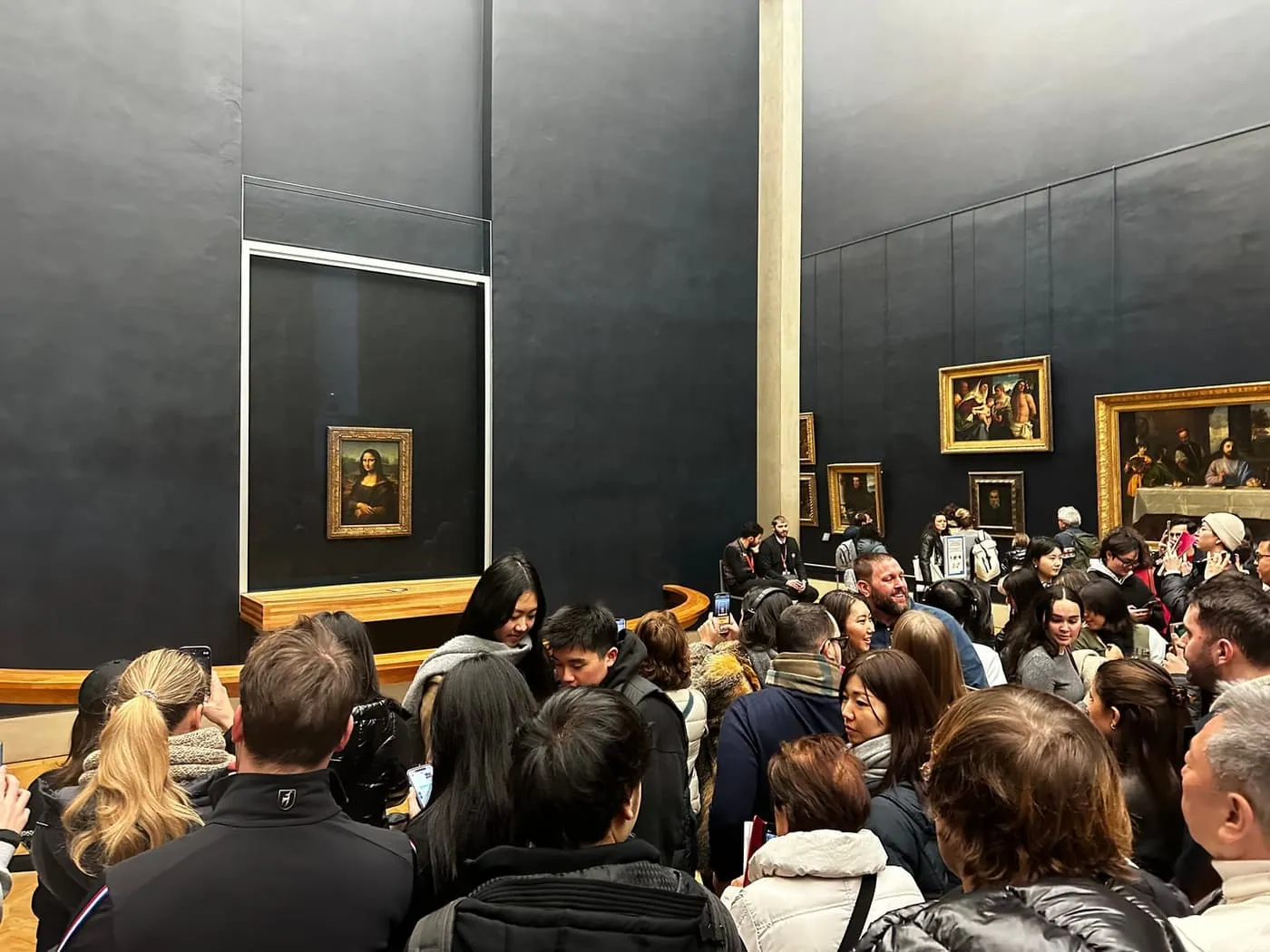 A crowd of visitors in front of the Mona Lisa behind its glass case in the Salle des États