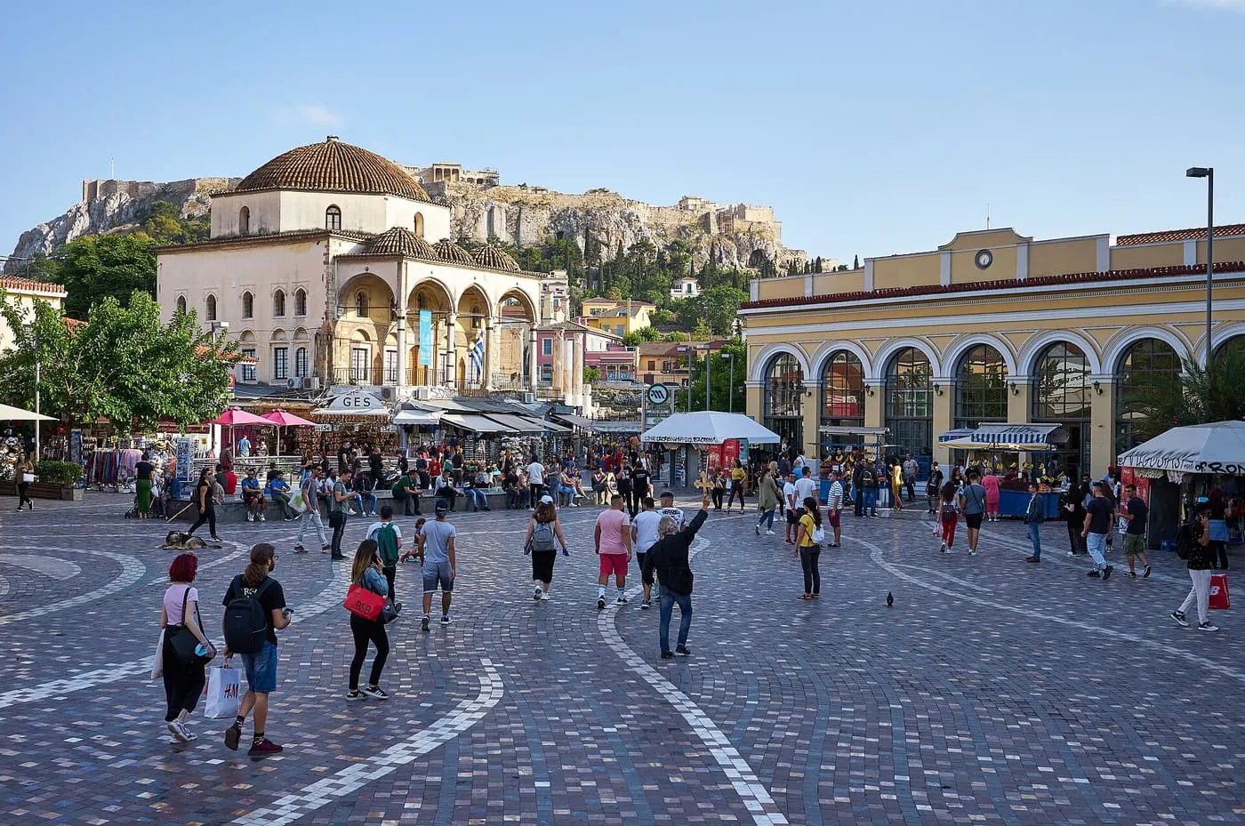 Monastiraki Square, a wide paved square with the domed Tzistarakis Mosque, the yellow station building and the Acropolis rock above the roofs