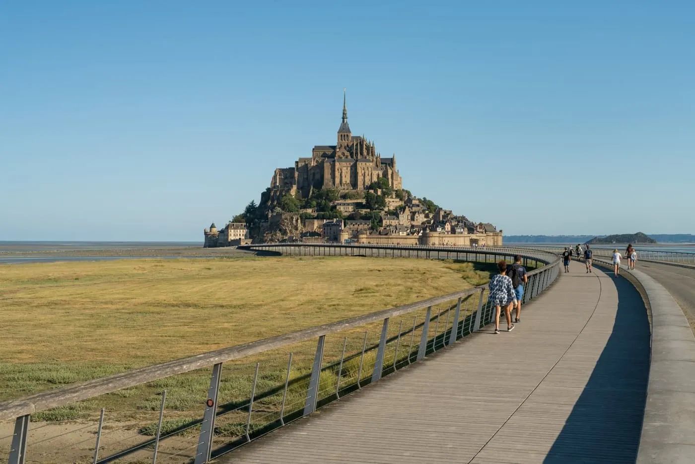 Visitors walking along the raised walkway across the salt meadows towards Mont-Saint-Michel