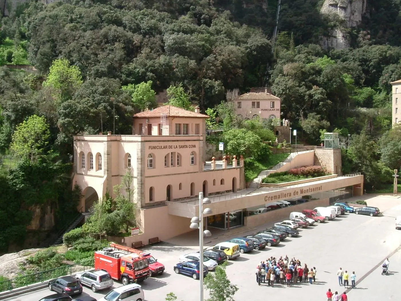 The pink Cremallera de Montserrat station at the monastery, with the Santa Cova funicular building beside it and wooded cliffs behind