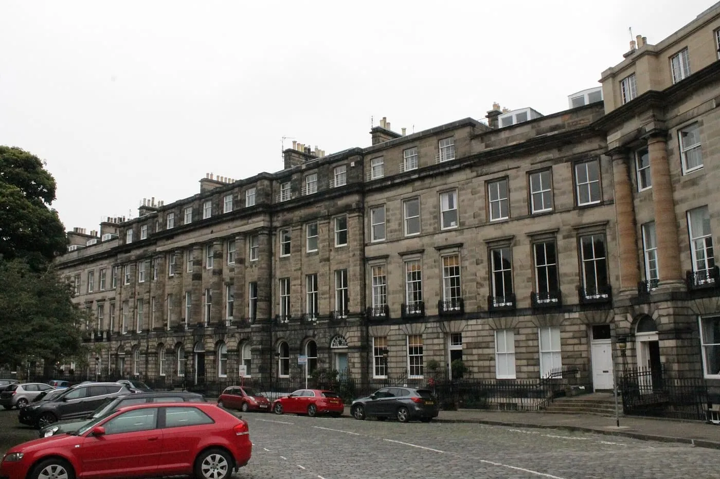 A long terrace of Georgian townhouses curving along cobbled Moray Place in the New Town, with cars parked at the kerb