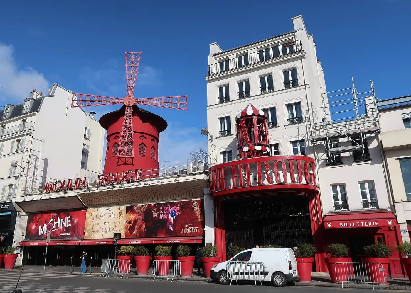 The red windmill and curved entrance of the Moulin Rouge on boulevard de Clichy, seen in daylight under a blue sky