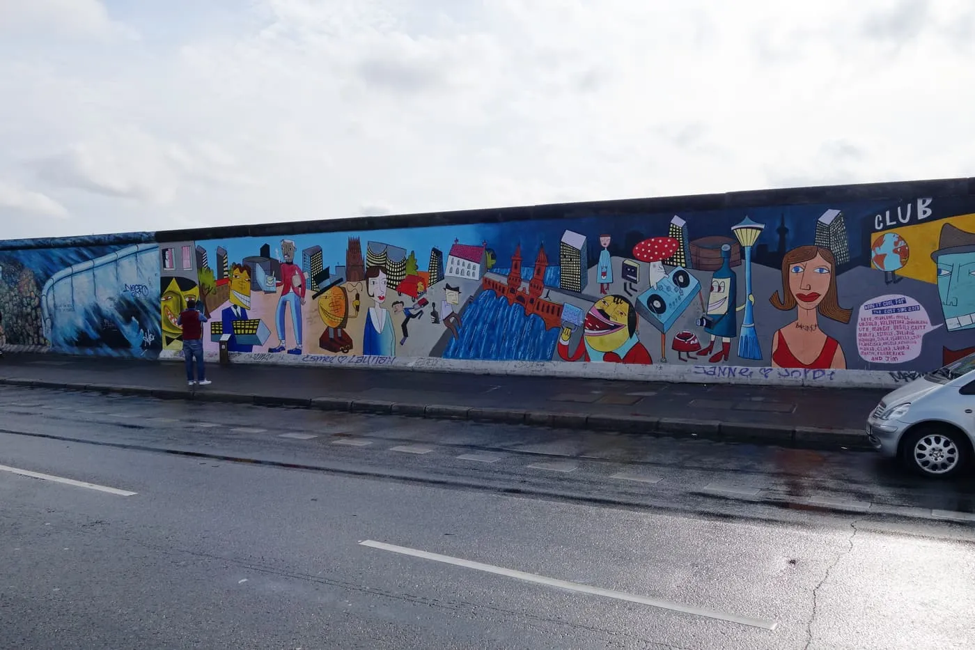 A stretch of the East Side Gallery along Mühlenstraße, a long painted section of the Wall showing cartoon figures, a bridge and tower blocks