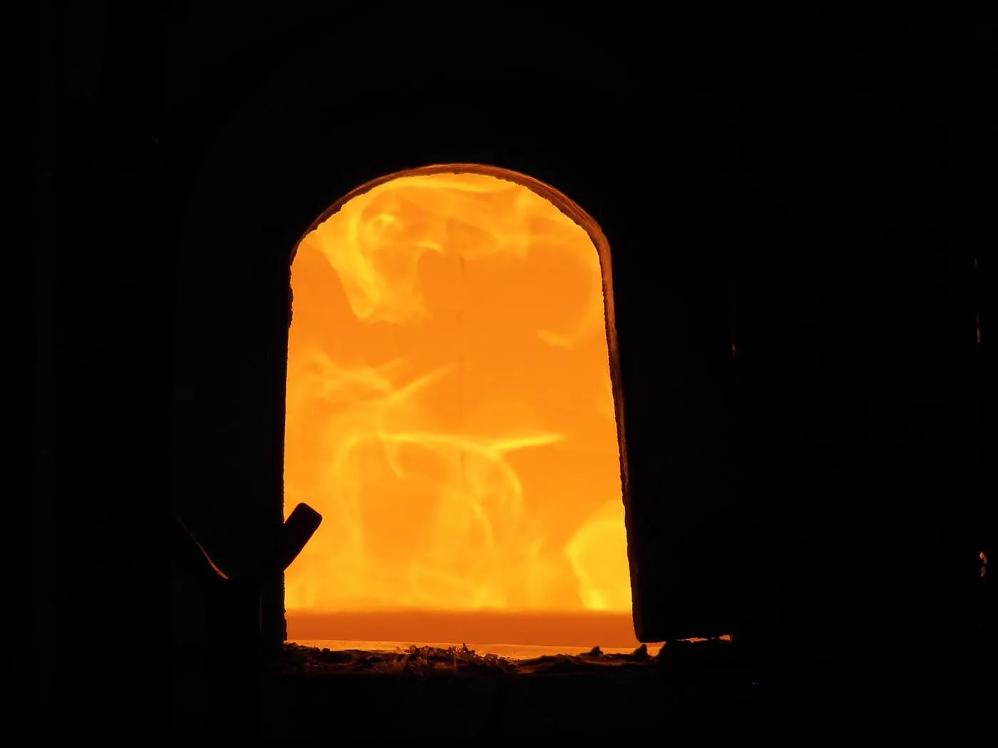 The glowing arched mouth of a glass furnace in a dark workshop