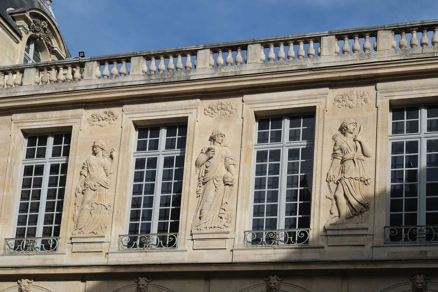 Carved stone figures in relief between the tall windows of the courtyard of the Hôtel Carnavalet, under a balustrade