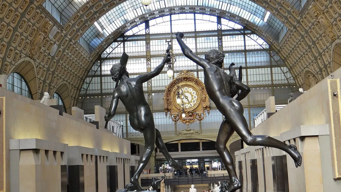 The central hall of the Musée d'Orsay, with two bronze figures in the foreground and the gilded station clock beneath the glass roof