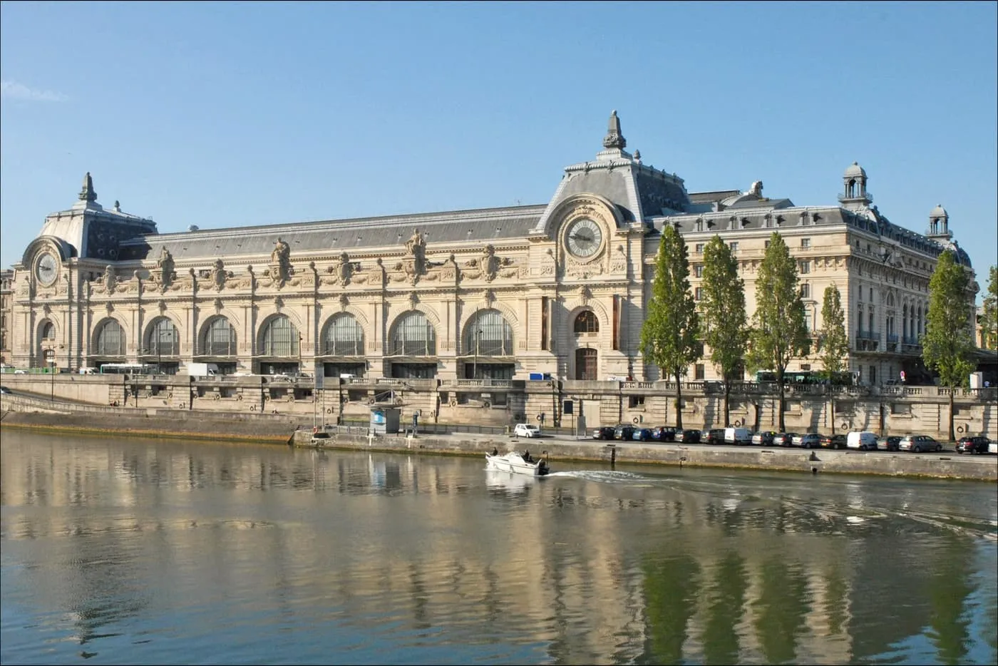 The long glazed front and two clock faces of the Musée d'Orsay, seen across the Seine under a clear blue sky