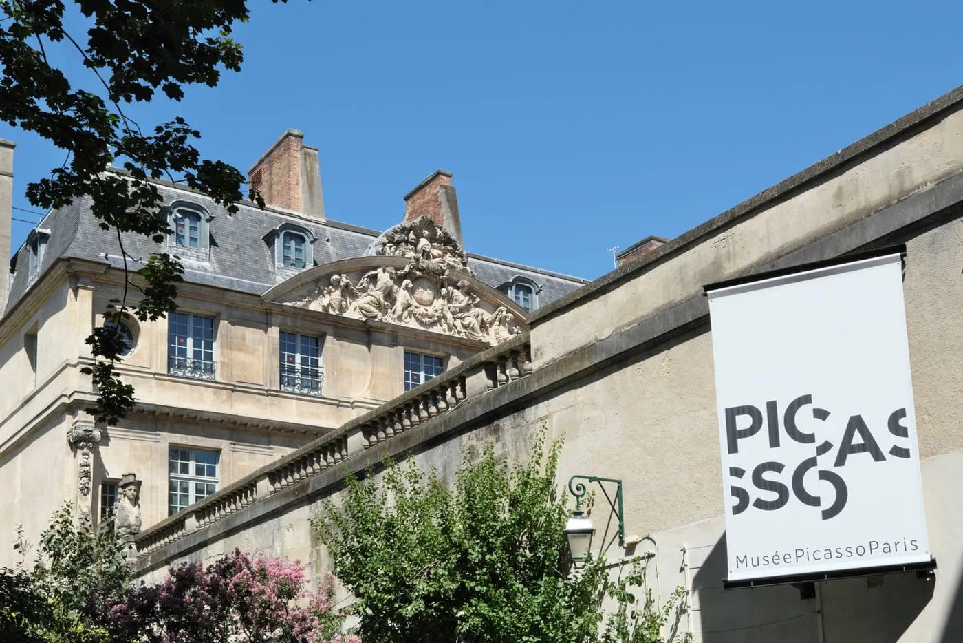 The carved stone pediment and slate roof of the Hôtel Salé behind a wall, with the Musée Picasso banner on the right