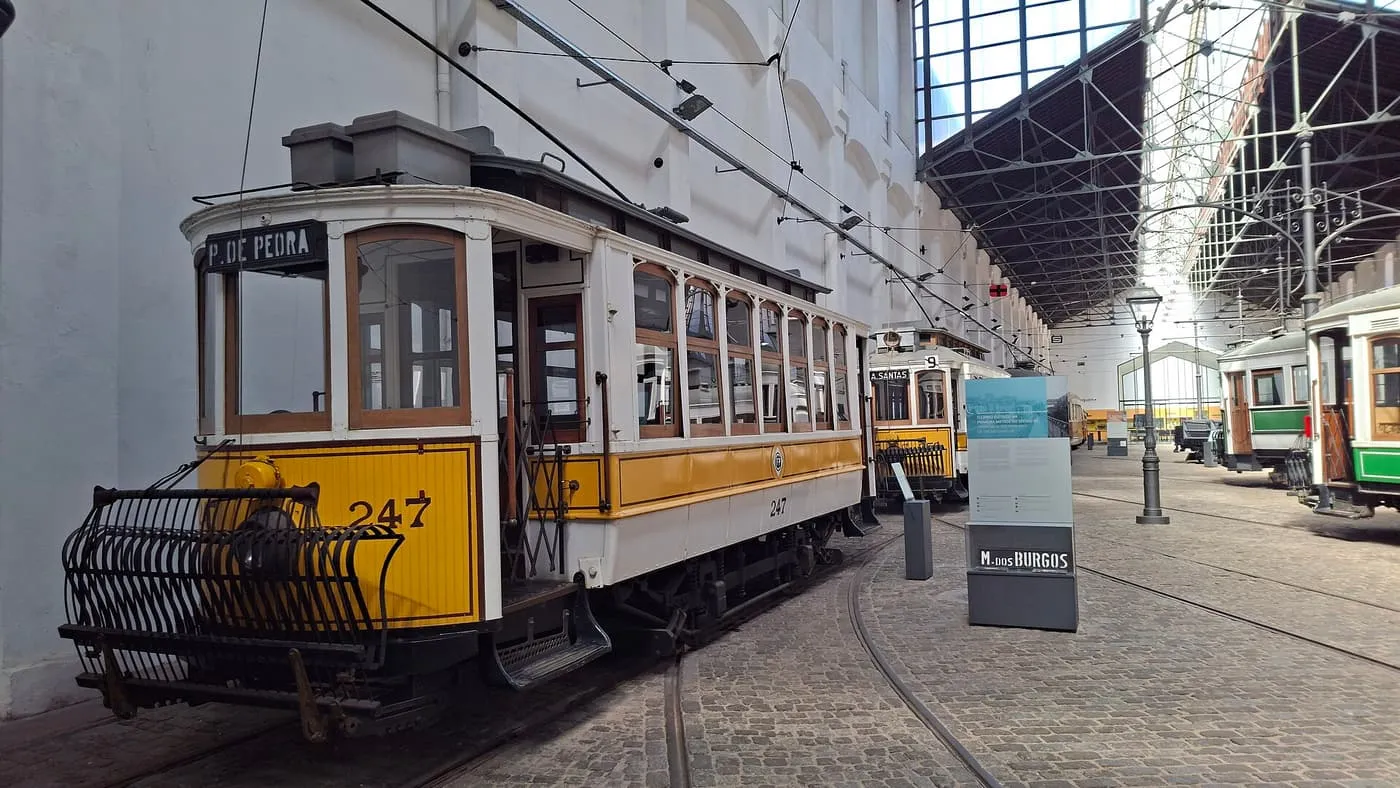 A yellow and white historic tram, number 247, on a track inside the glass-roofed hall of the Museu do Carro Eléctrico, with other trams beyond