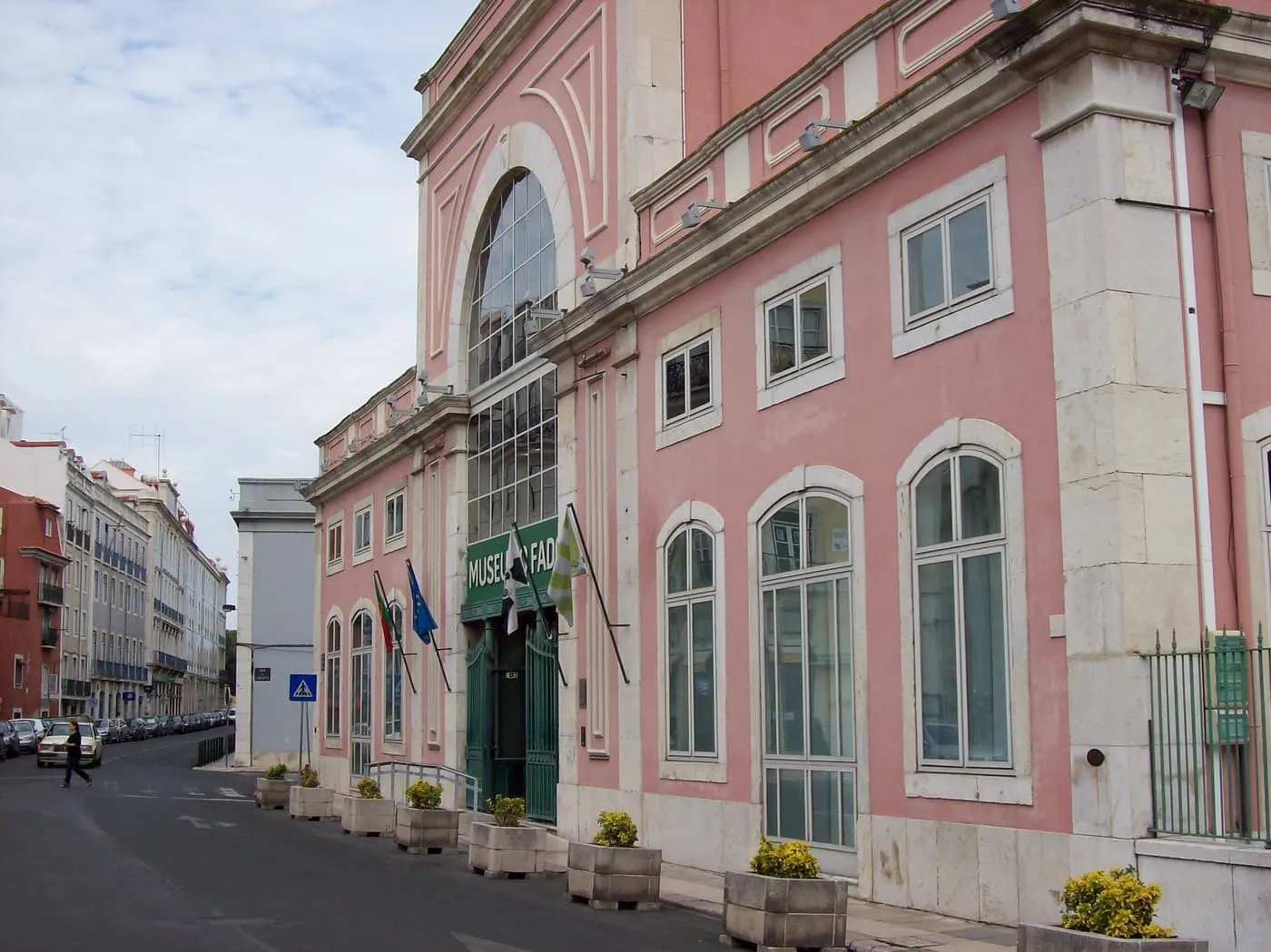 The pink front of the Museu do Fado, a former pumping station, with a tall arched window and a green entrance