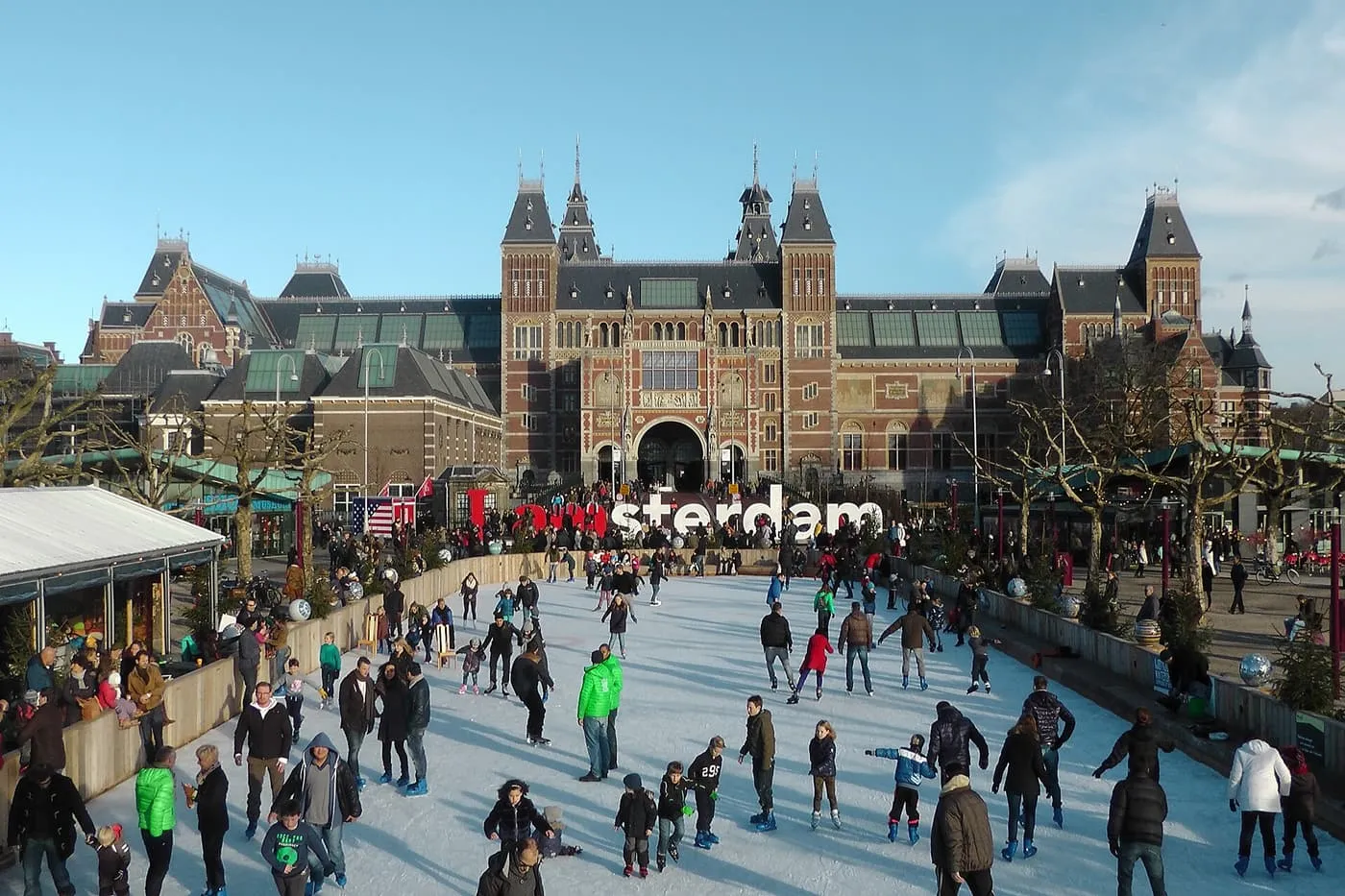 Skaters on the Museumplein ice rink in winter sun, with the Rijksmuseum and the I amsterdam letters behind