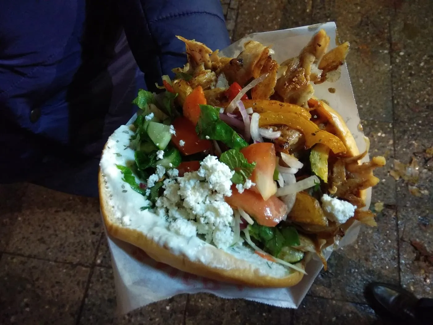 A chicken döner in flatbread with roast vegetables, salad, feta and yoghurt sauce, held in a paper wrapper