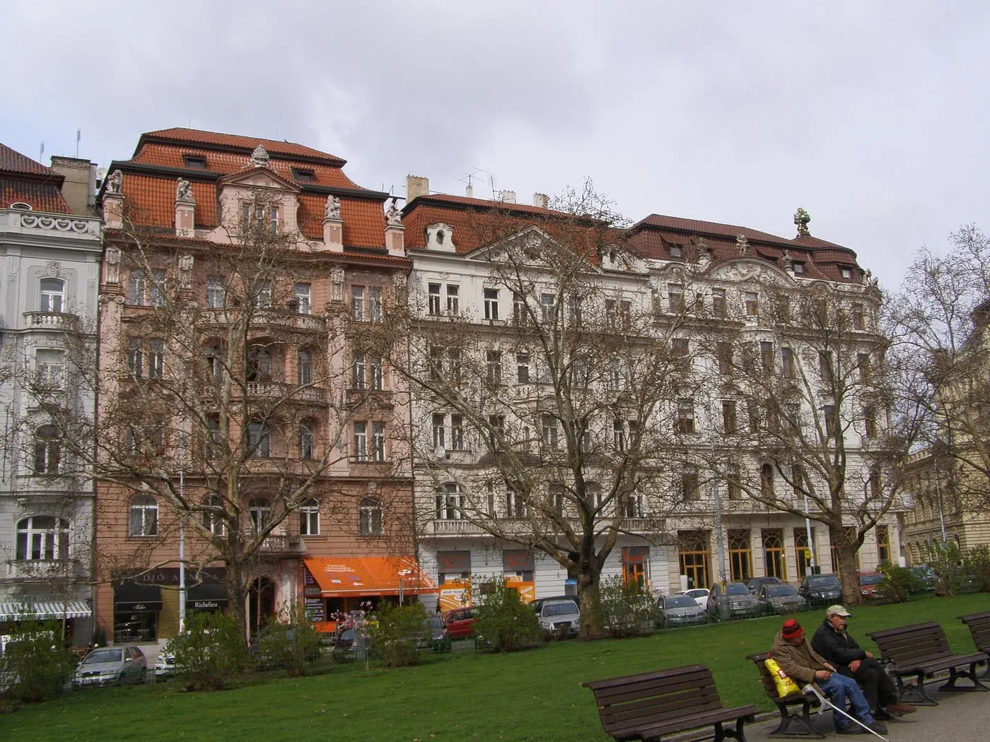 Ornate townhouses with red-tiled roofs facing a park with bare plane trees and benches on Náměstí Míru in Vinohrady