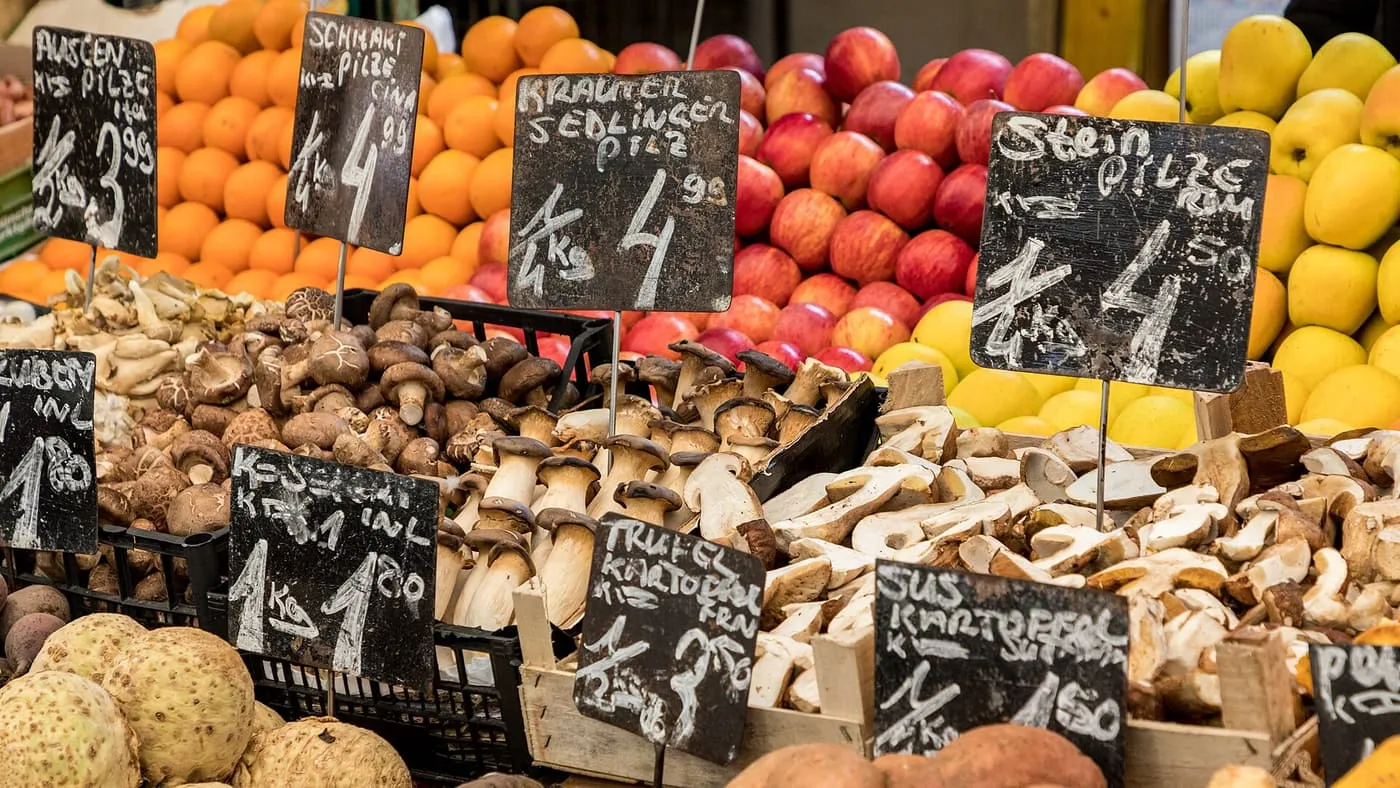 A Naschmarkt stall with loose mushrooms, apples and oranges under hand-lettered chalkboard price tags