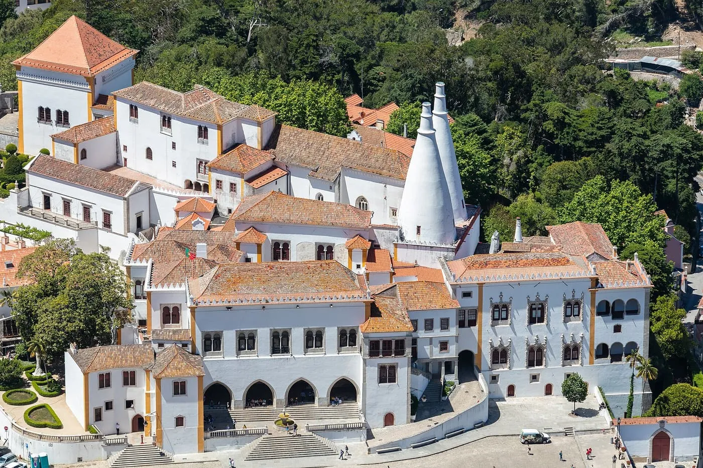 Aerial view of the white National Palace of Sintra, with two tall conical chimneys above its tiled roofs and the town square below