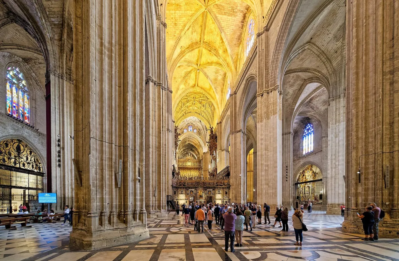 Visitors between the Cathedral's tall stone piers, with the choir and a gilded vault ahead