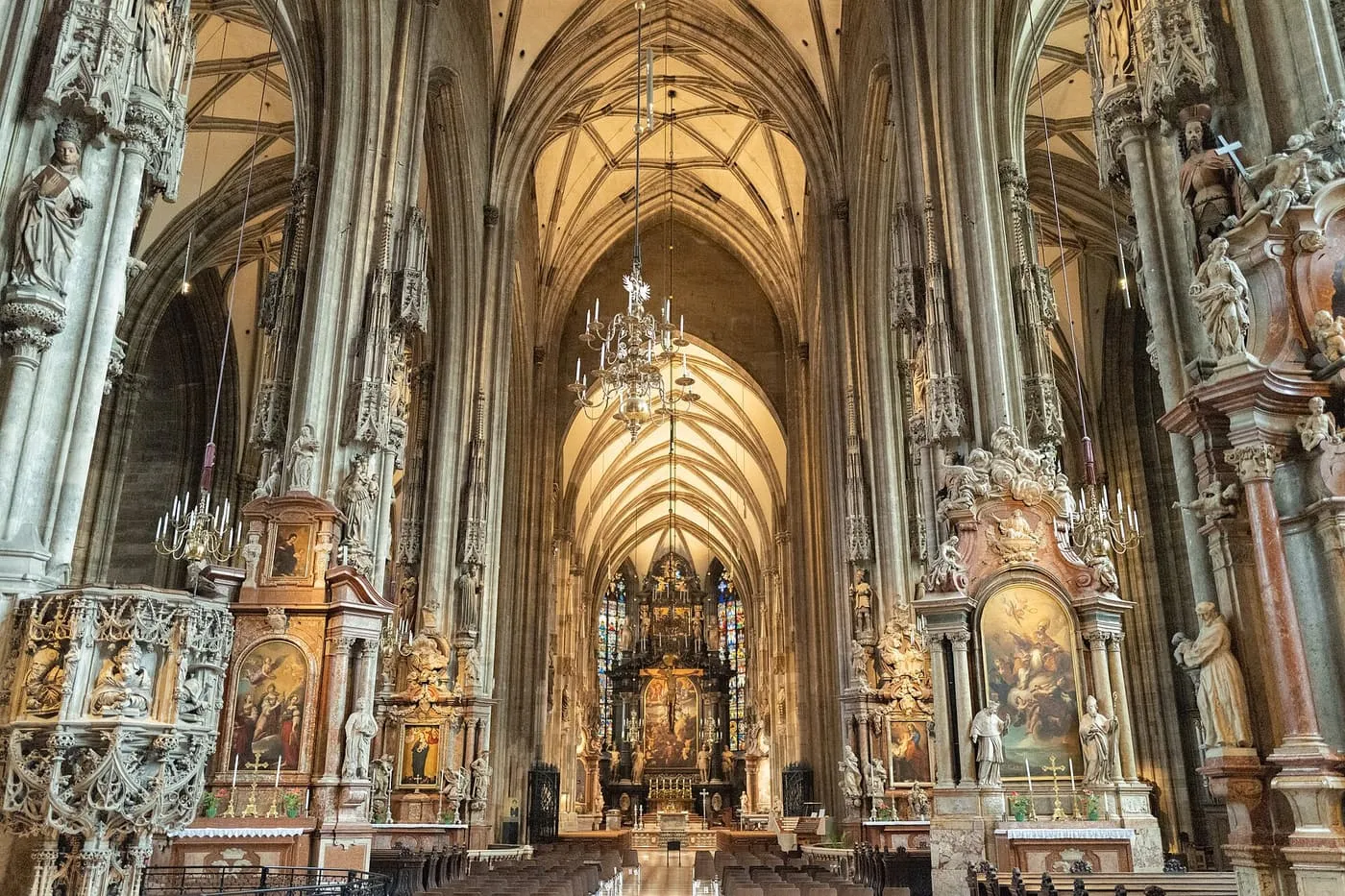 The nave of St Stephen's Cathedral, with ribbed Gothic vaults, a carved stone pulpit on the left and side altars along the columns