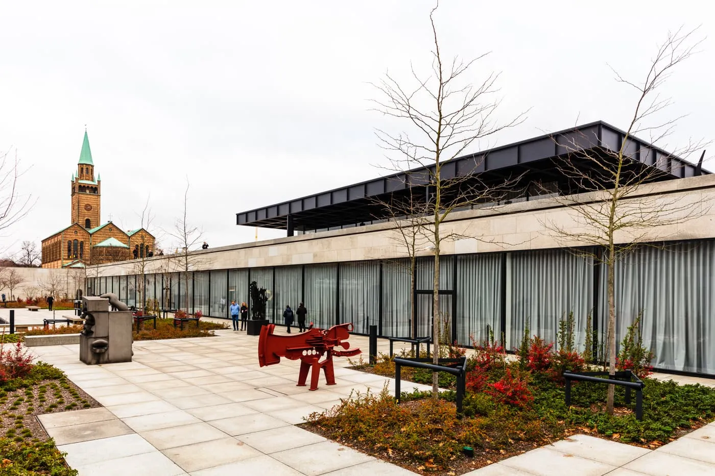 The Neue Nationalgalerie, with its black steel roof over a glass hall, seen across the sculpture garden with St Matthew's Church behind