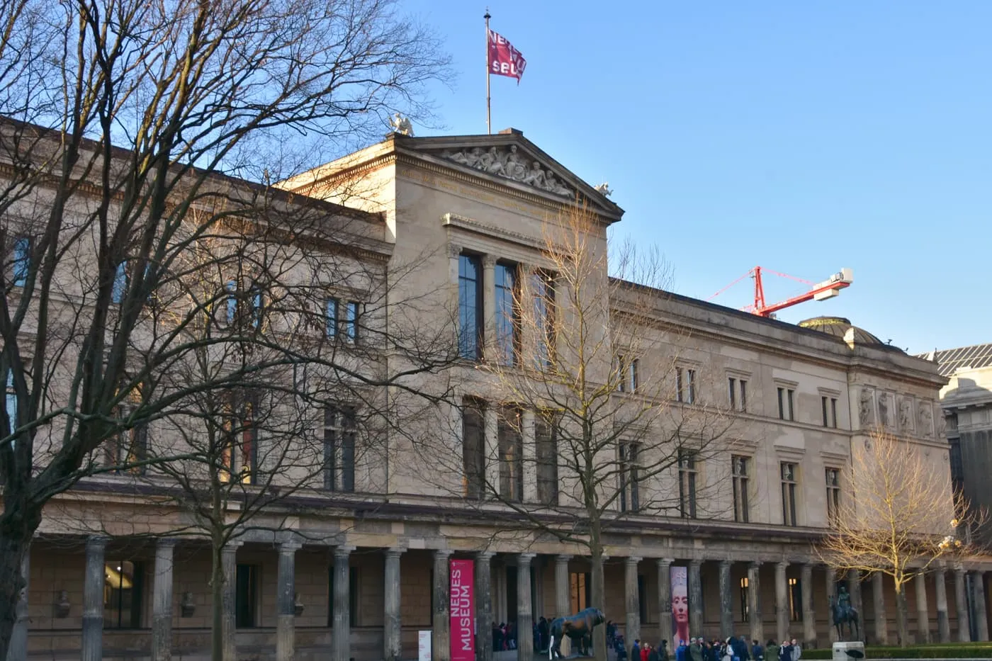 The Neues Museum on Museum Island, with its pediment and flag above a colonnade and bare winter trees in front