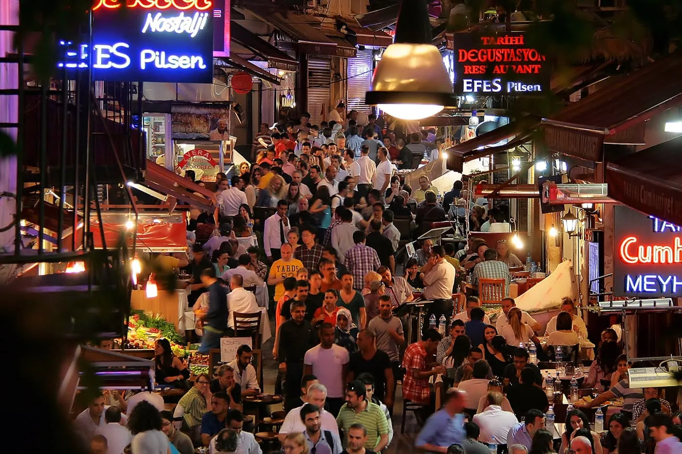 Nevizade Sokağı at night, packed with tables under neon signs and string lights