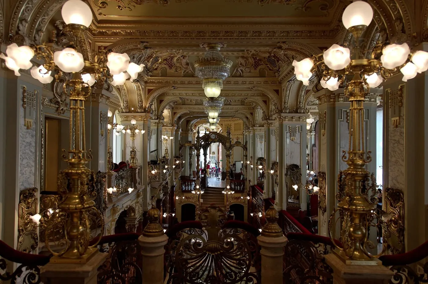The gilded hall of the New York Café, with brass lamps and ornate balustrades under a painted ceiling