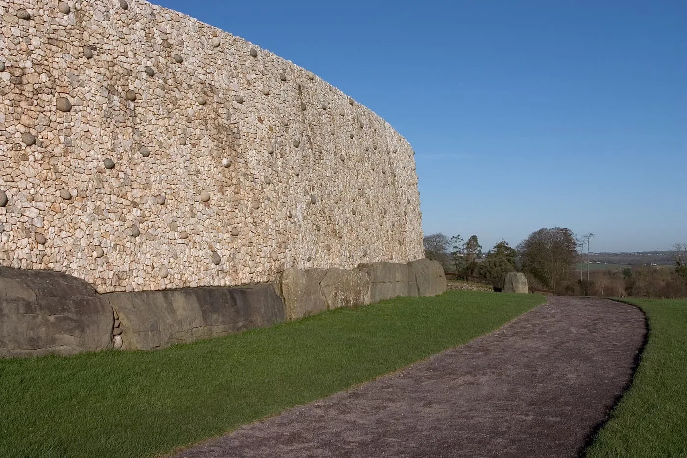 A curved wall of white quartz cobbles studded with rounded grey stones above a row of large kerbstones, beside a gravel path