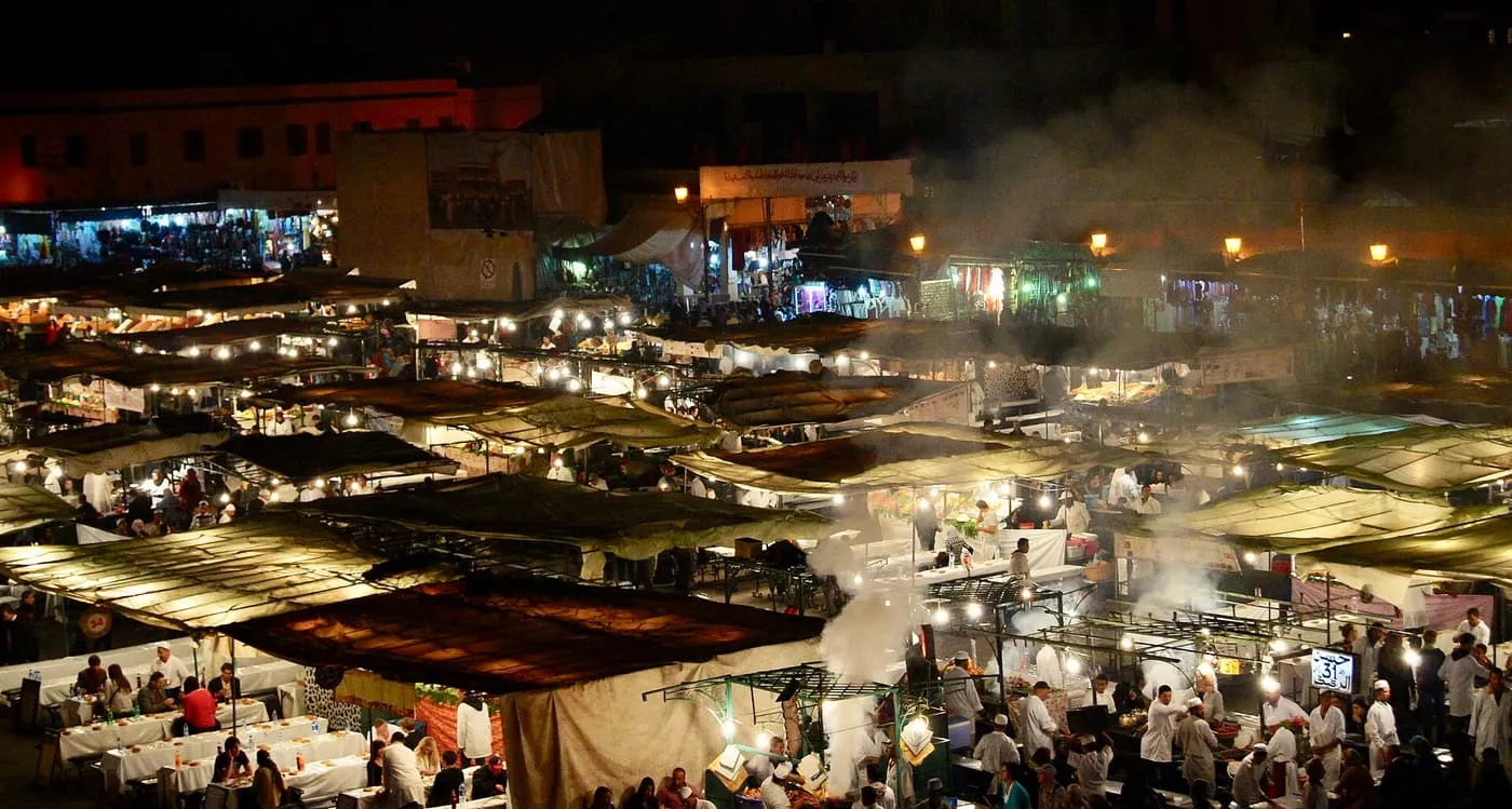 The food stalls of Jemaa el-Fnaa at night from above, with smoke rising over rows of lit awnings and diners at long tables