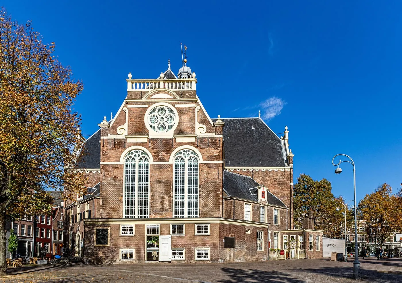The brick Noorderkerk, with a white-framed round window, two tall arched windows and a small tower, seen across the Noordermarkt under a blue sky