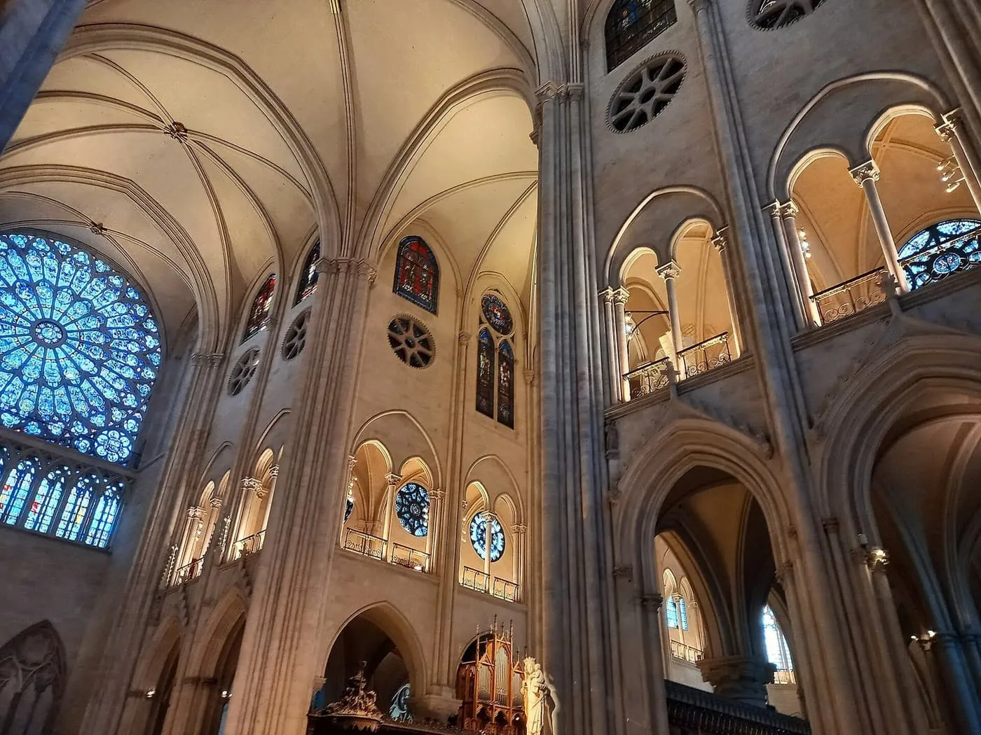 Looking up inside Notre-Dame at the pale ribbed vaults, a stained-glass rose window and the lit triforium galleries