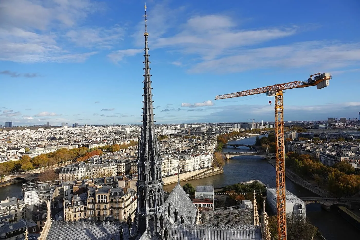 The spire of Notre-Dame rising above the lead roof, with the Seine, its bridges and a yellow construction crane beyond