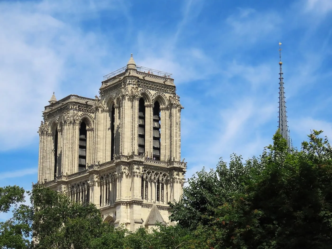 The towers of Notre-Dame with visitors on the platform at the top, and the spire rising beyond the trees