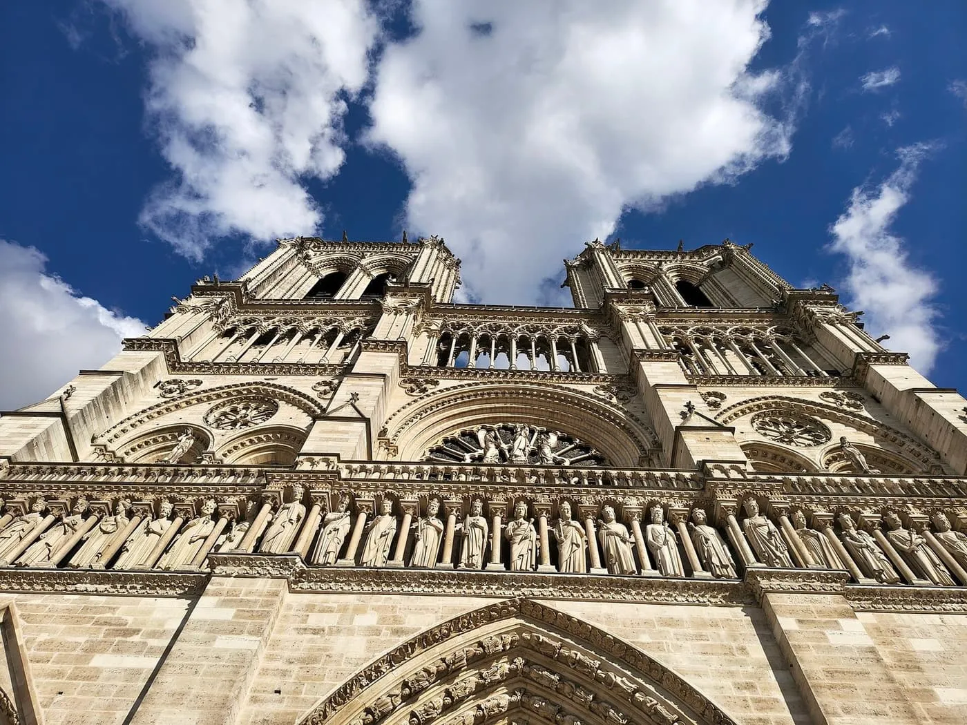 Looking up the west front of Notre-Dame de Paris, with the Gallery of Kings, the rose window and both towers against a blue sky