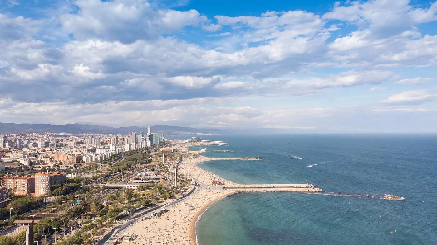 Aerial view along the Barcelona coast, with the sand of the Nova Icària and Bogatell beaches and their breakwaters curving away towards the Fòrum