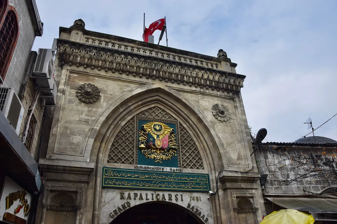 A gate of the Grand Bazaar: a pointed stone arch with a gilded Ottoman coat of arms, a green inscription panel and a Turkish flag on top