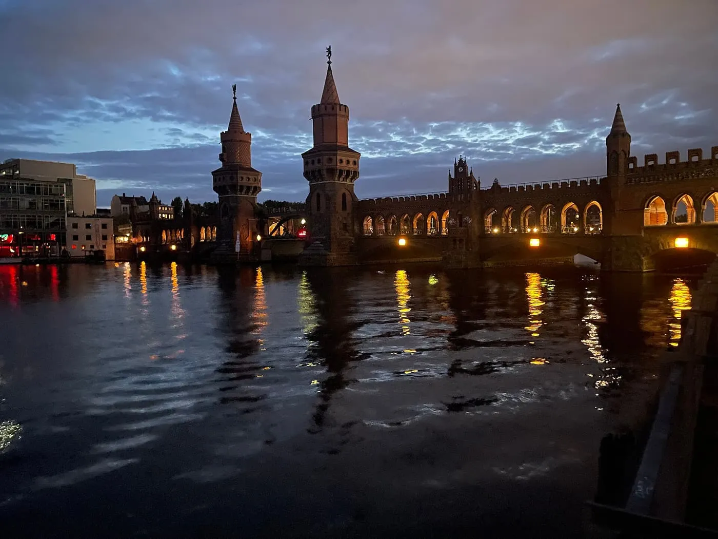 The brick towers and arcaded roadway of the Oberbaumbrücke lit up over the Spree after sunset