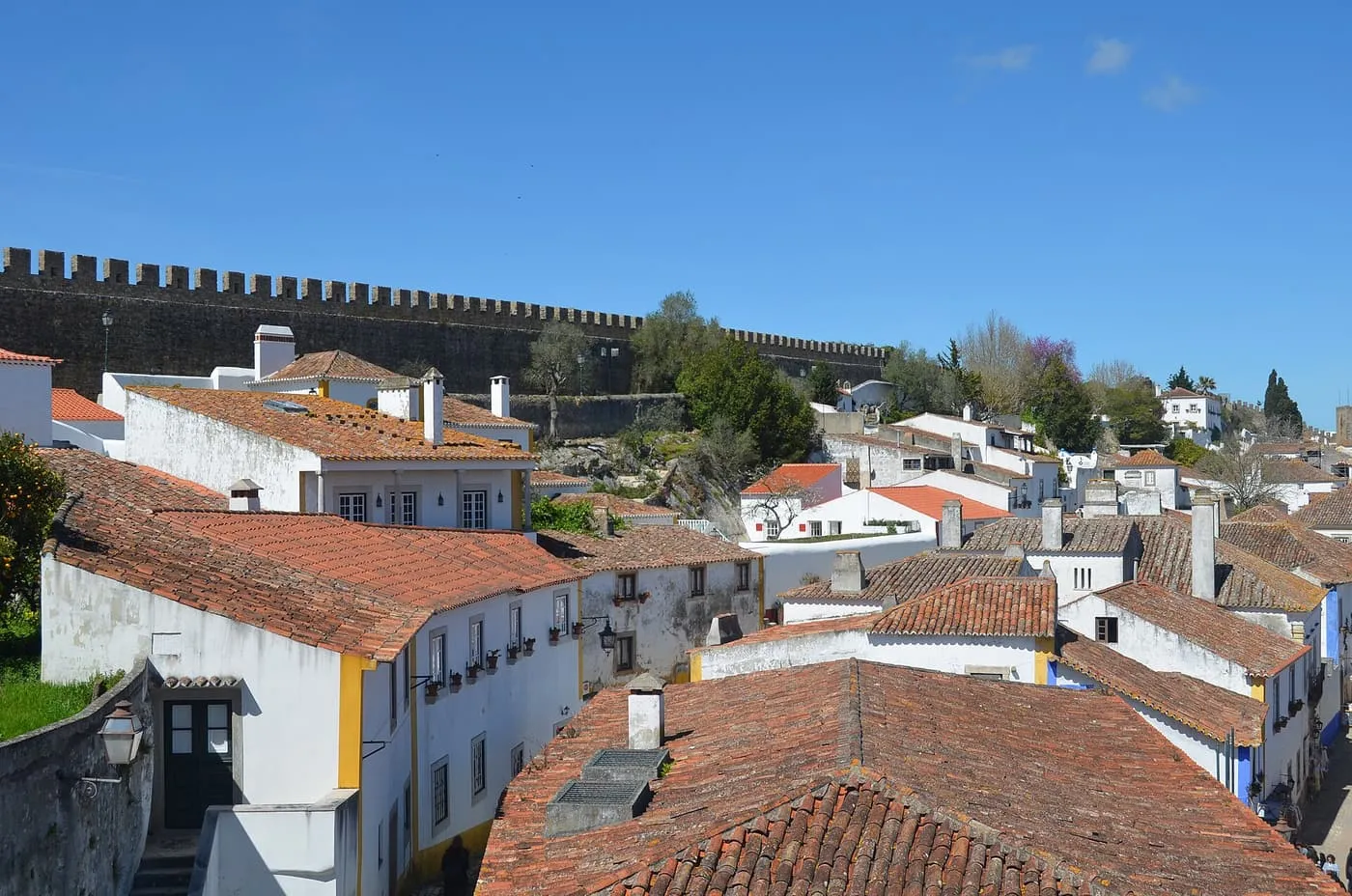 Terracotta roofs and whitewashed houses below Óbidos's crenellated town walls, under a clear blue sky
