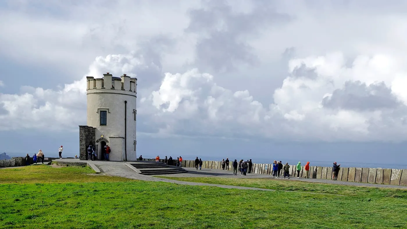 The round stone O'Brien's Tower with a crenellated top, visitors along the wall beside it and clouds behind