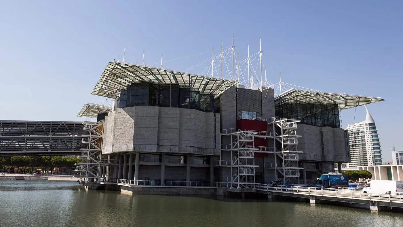 The Oceanário de Lisboa, a concrete and glass building on piers above the water, with white masts rising behind it