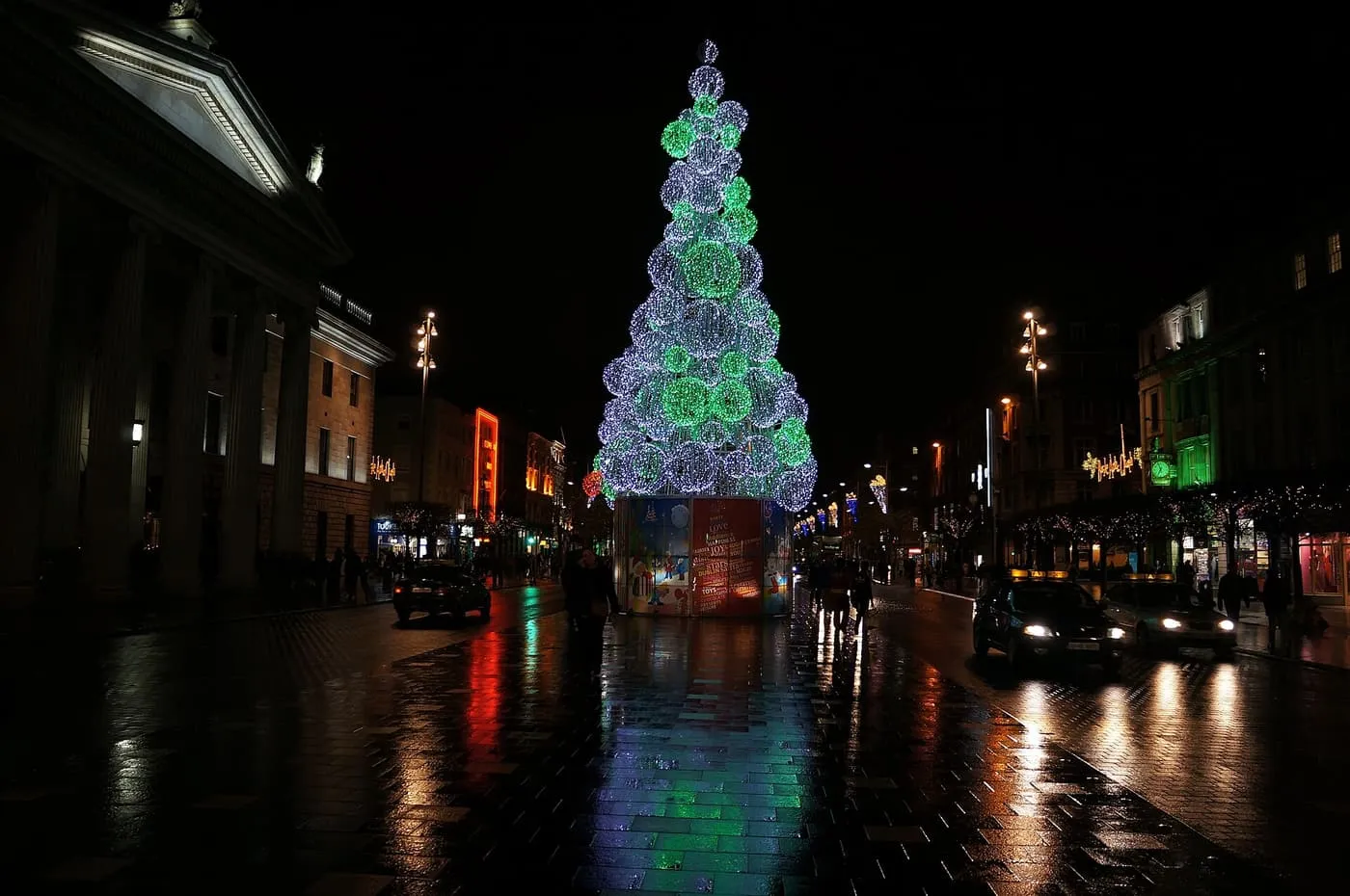 A tall Christmas tree of lit spheres in the middle of O'Connell Street at night, beside the columns of the General Post Office