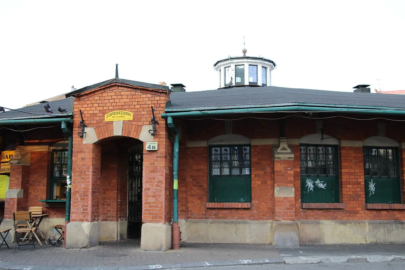 The Okrąglak on Plac Nowy, a low red-brick pavilion with green windows, a glazed lantern on its roof and a gate in a brick porch