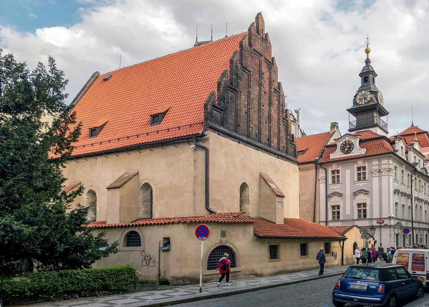 The Old-New Synagogue, a stepped brick gable above a low stone building with a red tiled roof, beside the white Jewish Town Hall with its clock tower