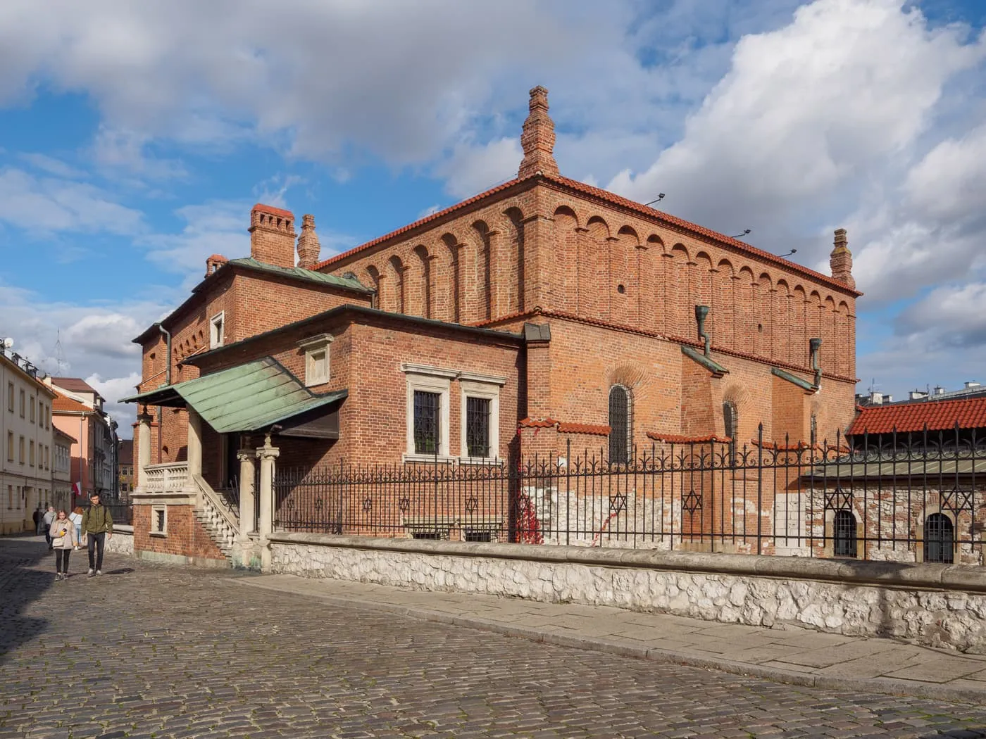 The Old Synagogue in Kazimierz, a red-brick building with a tiled roof, beside a cobbled street